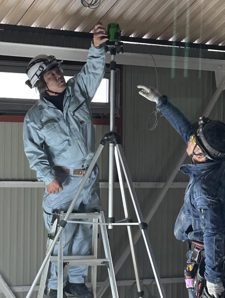 高所でレーザー墨出し器を使って水平位置の調整を行うY・Aさんと作業員