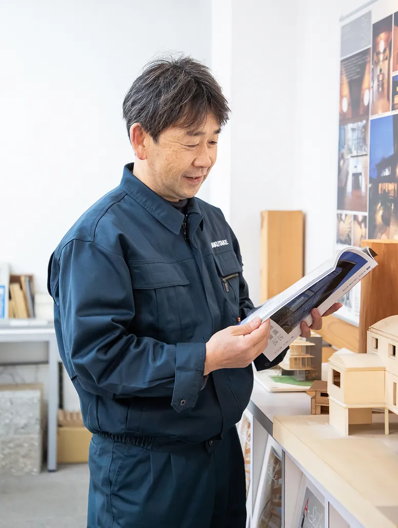 建築模型が並ぶ棚の前で、資料を手に取りリサーチをしているT・Sさん